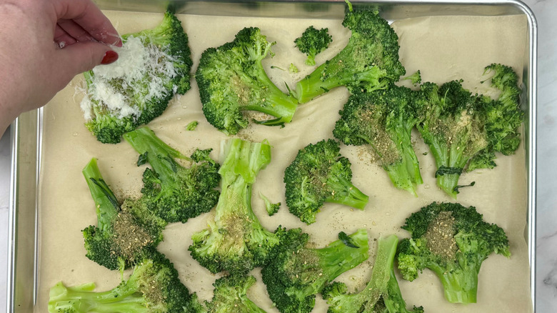 sprinkling parmesan on cooked broccoli on baking sheet