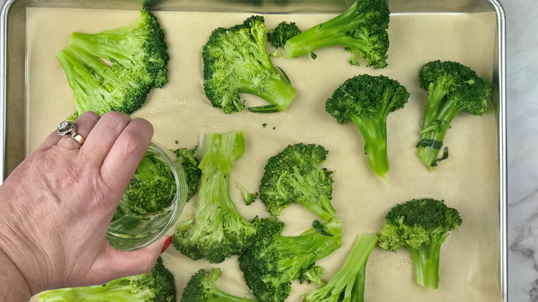 hand pressing cooked broccoli flat on baking sheet